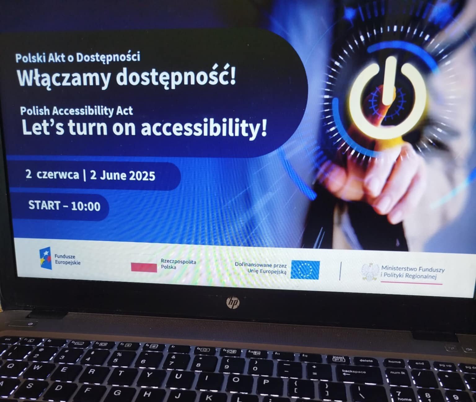 Na zdjęciu widać ekran laptopa z grafiką promującą konferencję „Polski Akt o Dostępności – Włączamy dostępność!”